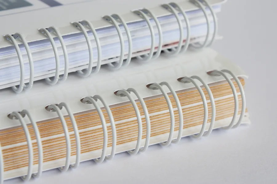 Gros plan sur deux brochures reliées en Wire’O blanc, paires de boucles métalliques passées dans des perforations carrées