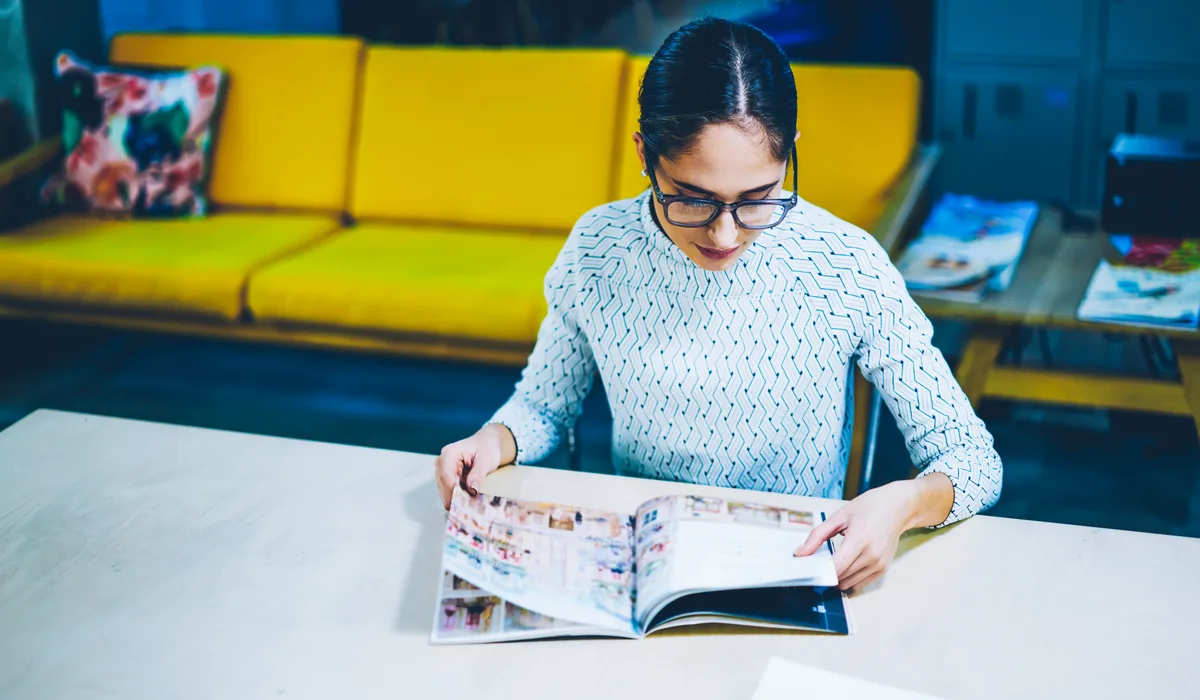 Acheteuse feuilletant un catalogue produits imprimé, ouvert sur une double page de références